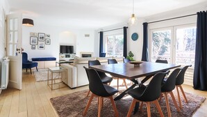 Un salon moderne avec un coin repas, comprenant une grande table en bois, des chaises noires, un canapé et un téléviseur.