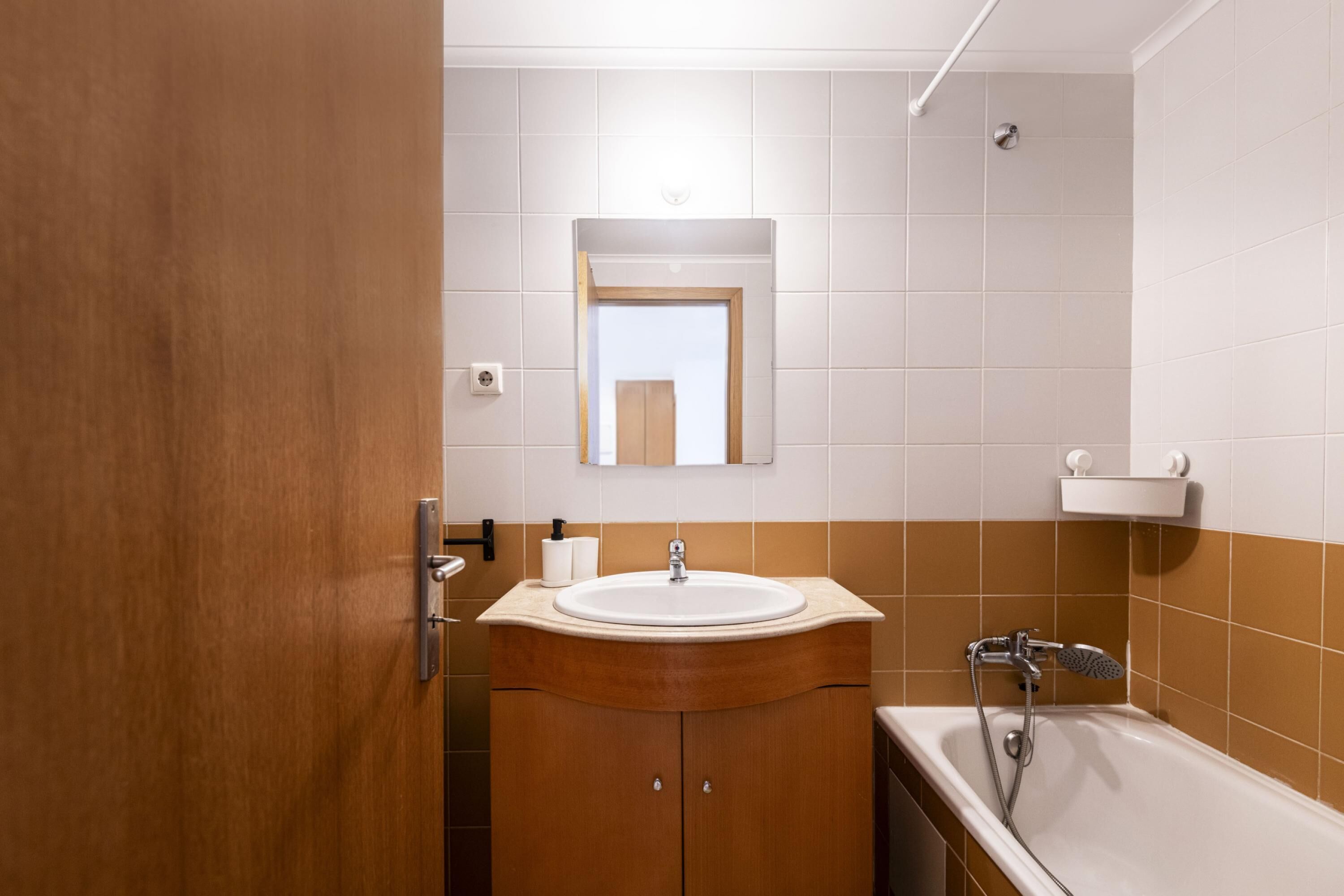 Un baño con tocador de madera, lavamanos, espejo, inodoro y bañera.