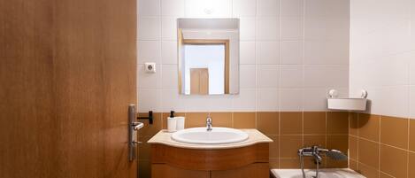 Un baño con tocador de madera, lavamanos, espejo, inodoro y bañera.