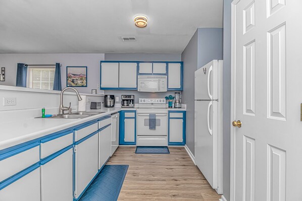Una cocina compacta con armarios blancos y azules, un microondas integrado, una estufa y un refrigerador.