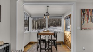 A dining area with a wooden table and chairs, large windows with a view of a snowy landscape, and a painting on the wall. - Cozy Townhome next to PC Resort! Stylish 2BR/2BA +loft, deck, +more (Park City)