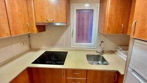 A compact kitchen with wooden cabinets, a stove, a sink, and a refrigerator. - Kai Etxea , el mismo puerto de Bermeo (Bermeo)