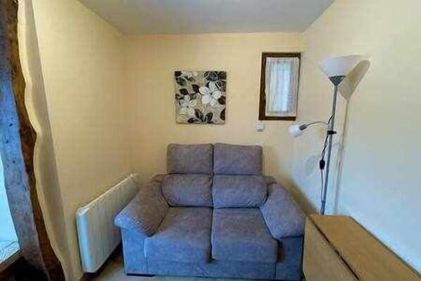 A small, compact room with a grey sofa, a radiator, a wall-mounted artwork, and a floor lamp.