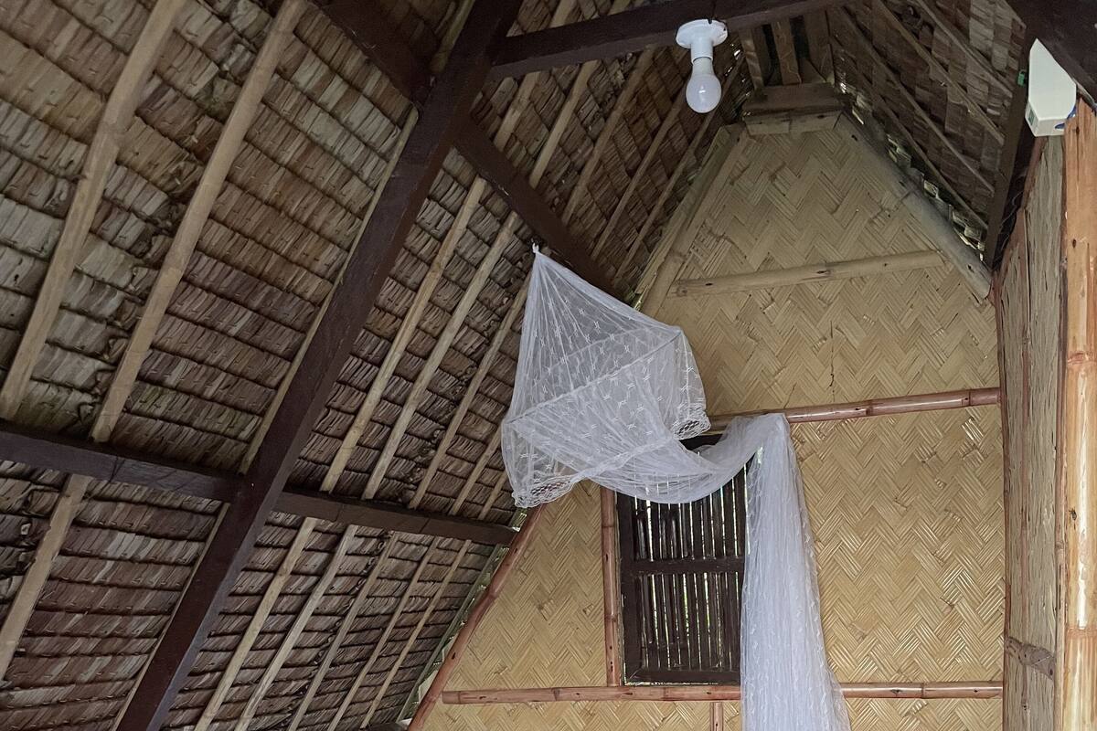 Una cama individual con ropa blanca en una habitación con techo de paja y paredes de madera.