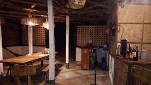 Ein rustikaler Innenraum mit freiliegenden Holzbalken, einem Holztisch, einer Bar mit Flaschen und einer Wand mit Muster.