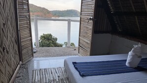 Ein Zimmer mit Bett, Seeblick und einem Strohdach.