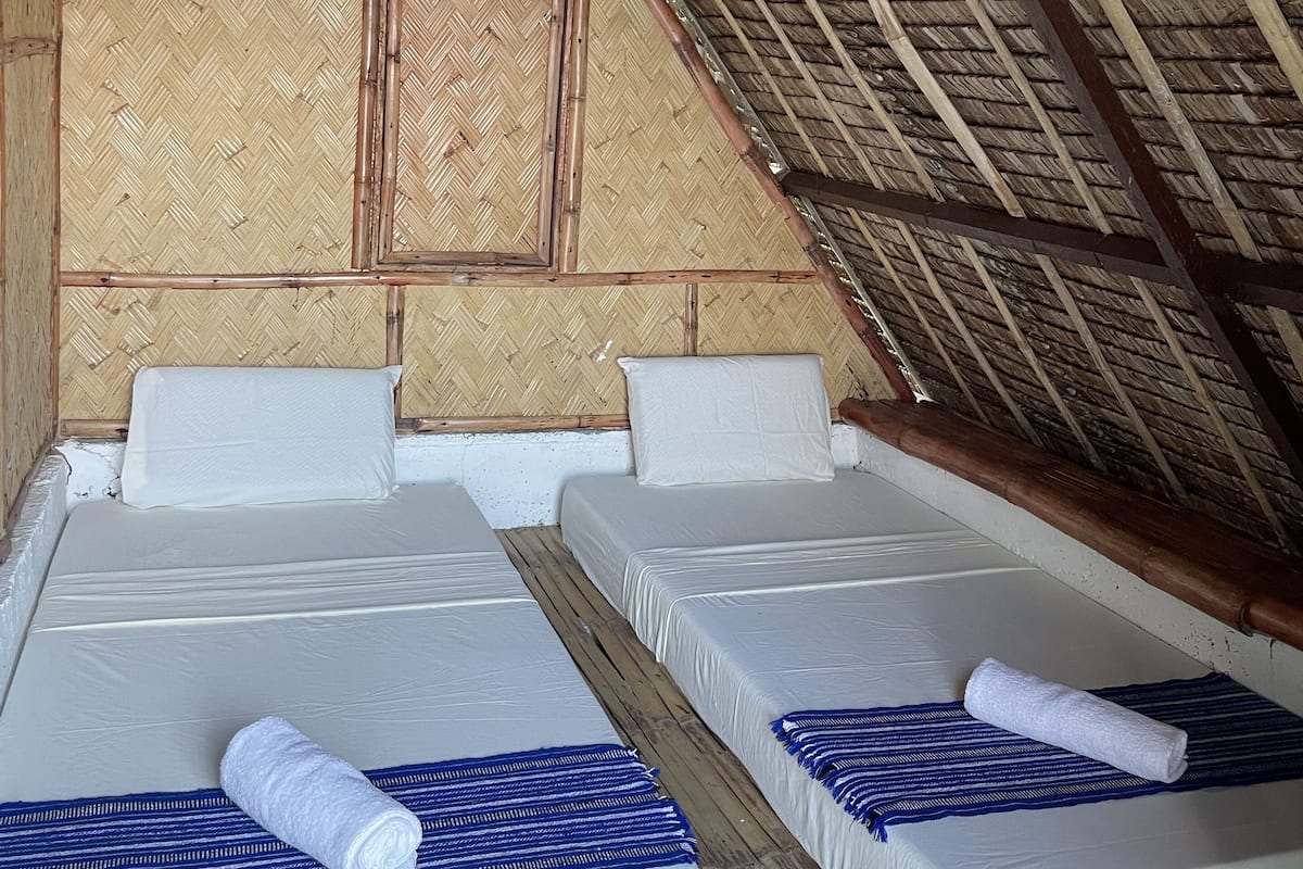 Una habitación con dos camas, techo de paja y pared con motivo de espiga.