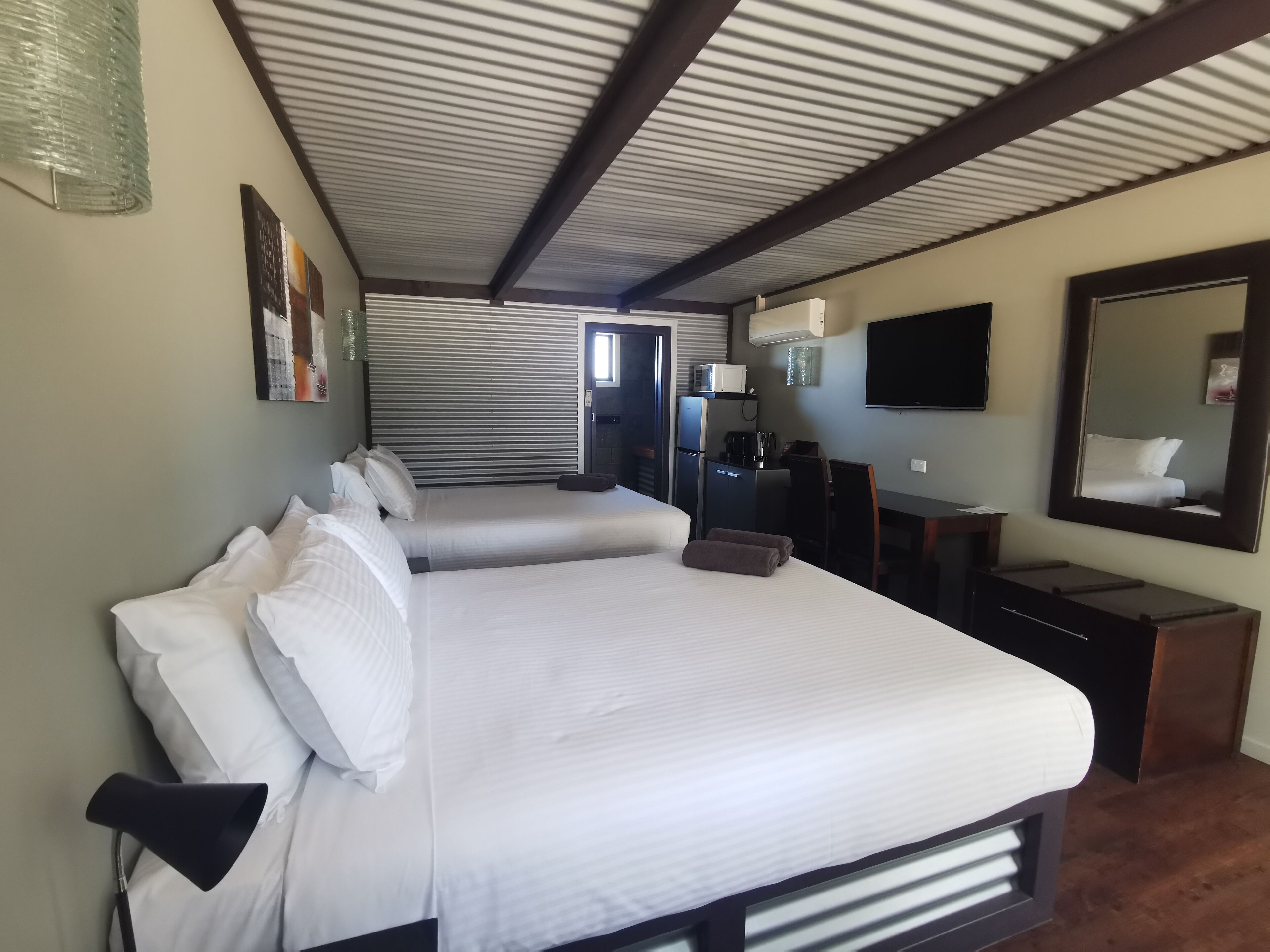 A hotel room with a large bed, a desk, a television, and a mirror.