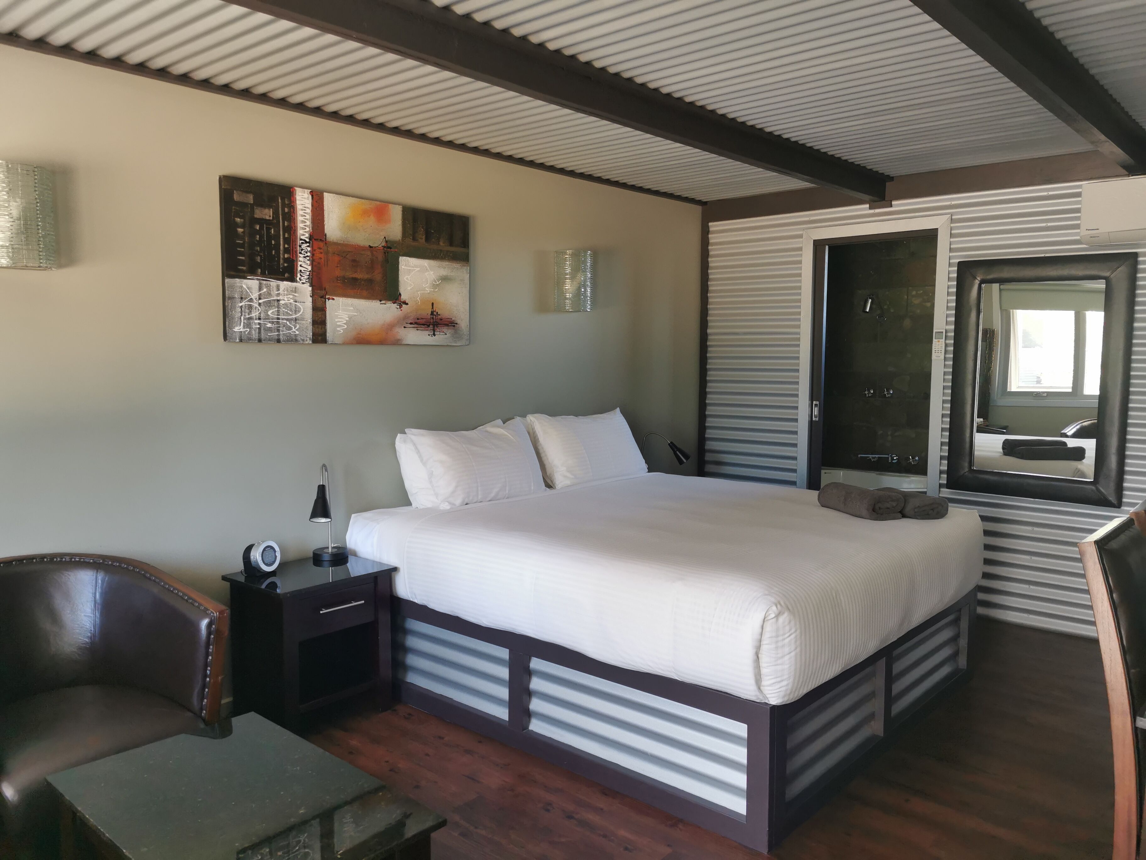 Un dormitorio con cama, mesita de noche, lámpara y un cuadro en la pared.