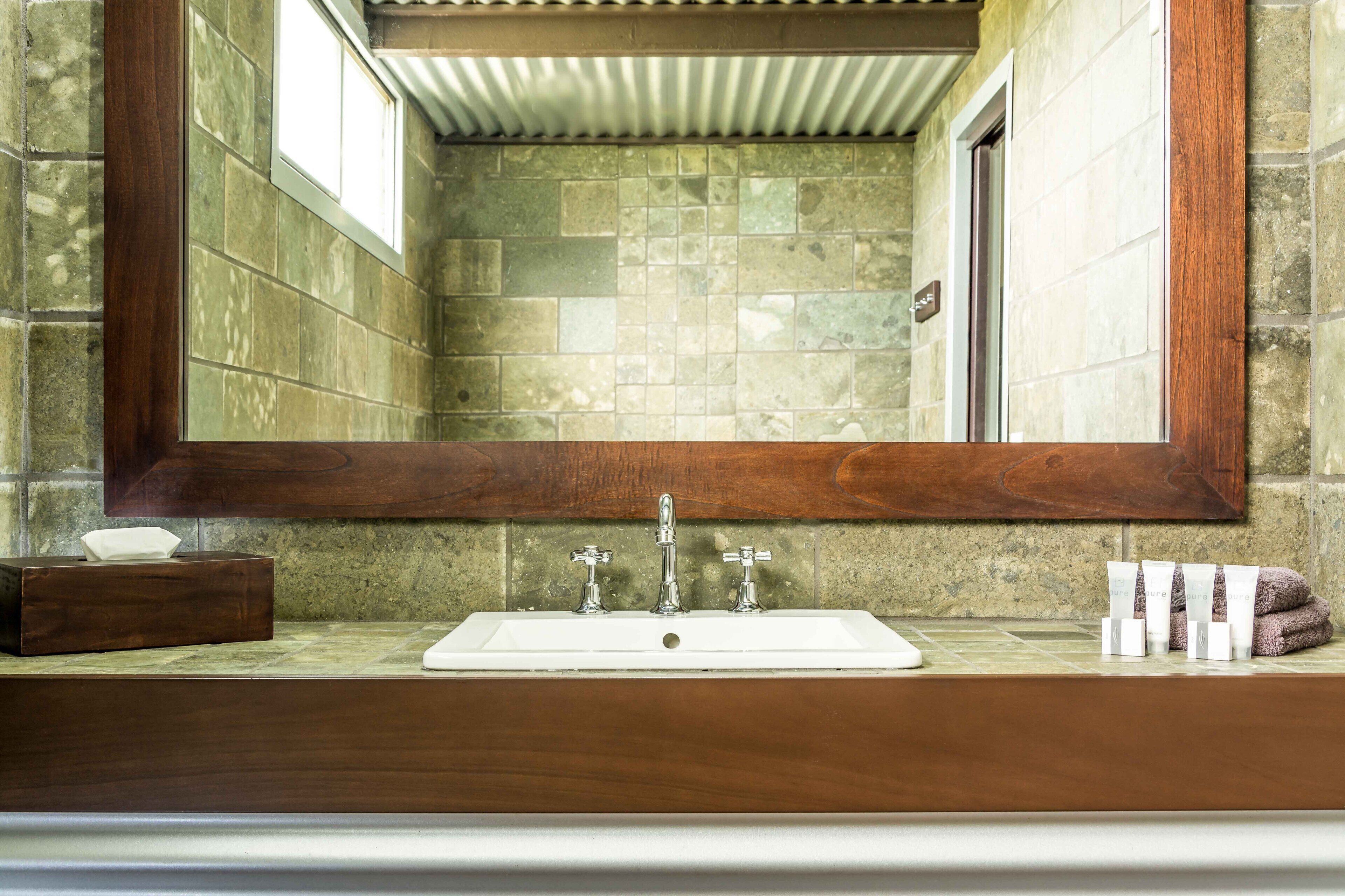 Een badkamer met een grote spiegel, een wastafel met twee kraan en een douchehoek.