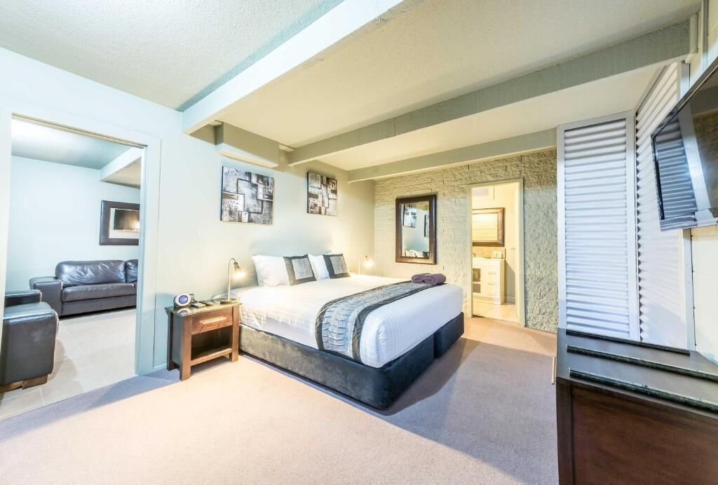 Een slaapkamer met een groot bed, een nachtkastje, een dressoir en een raam met jaloezieën.
