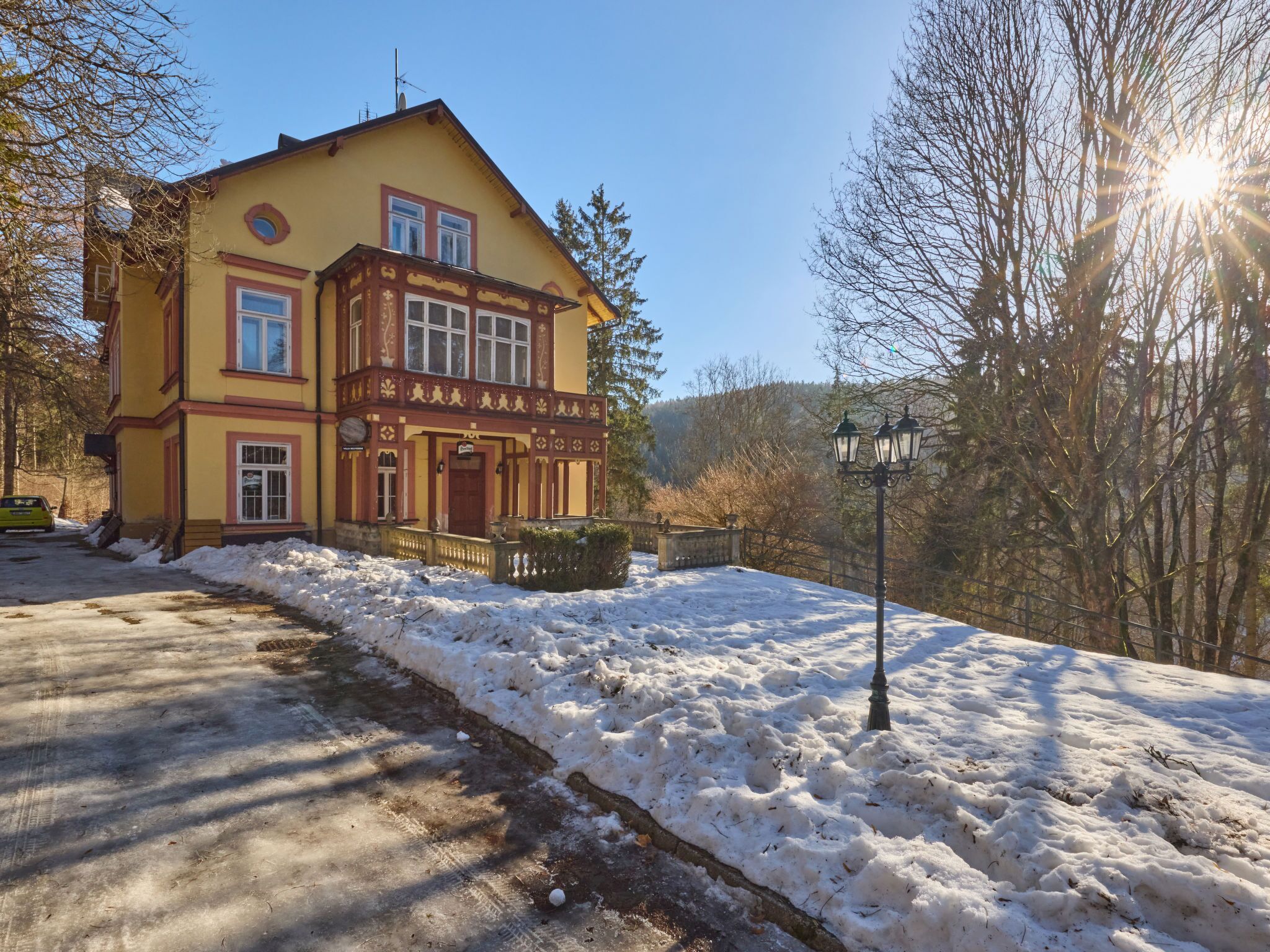 Un bâtiment à deux étages, doté d’une façade jaune et d’un balcon, entouré d’un paysage enneigé et d’arbres.