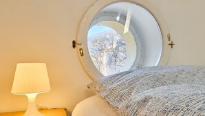 Une chambre avec une fenêtre ronde, une table de chevet avec une lampe et un lit avec une literie à motifs.