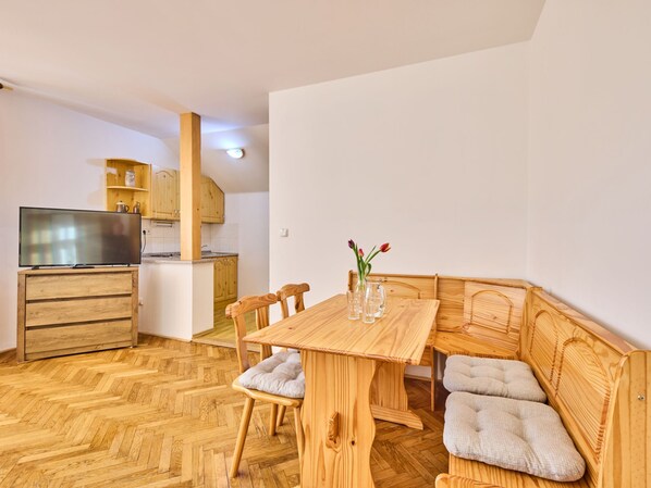 Un espace de vie compact comprenant une table à manger en bois, un canapé et un téléviseur, le tout aménagé dans un coin cuisine.