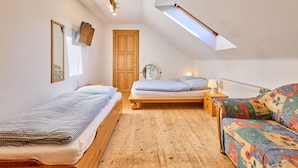 Quarto de sótão acolhedor com duas camas, um claraboia, piso de madeira e um sofá colorido.