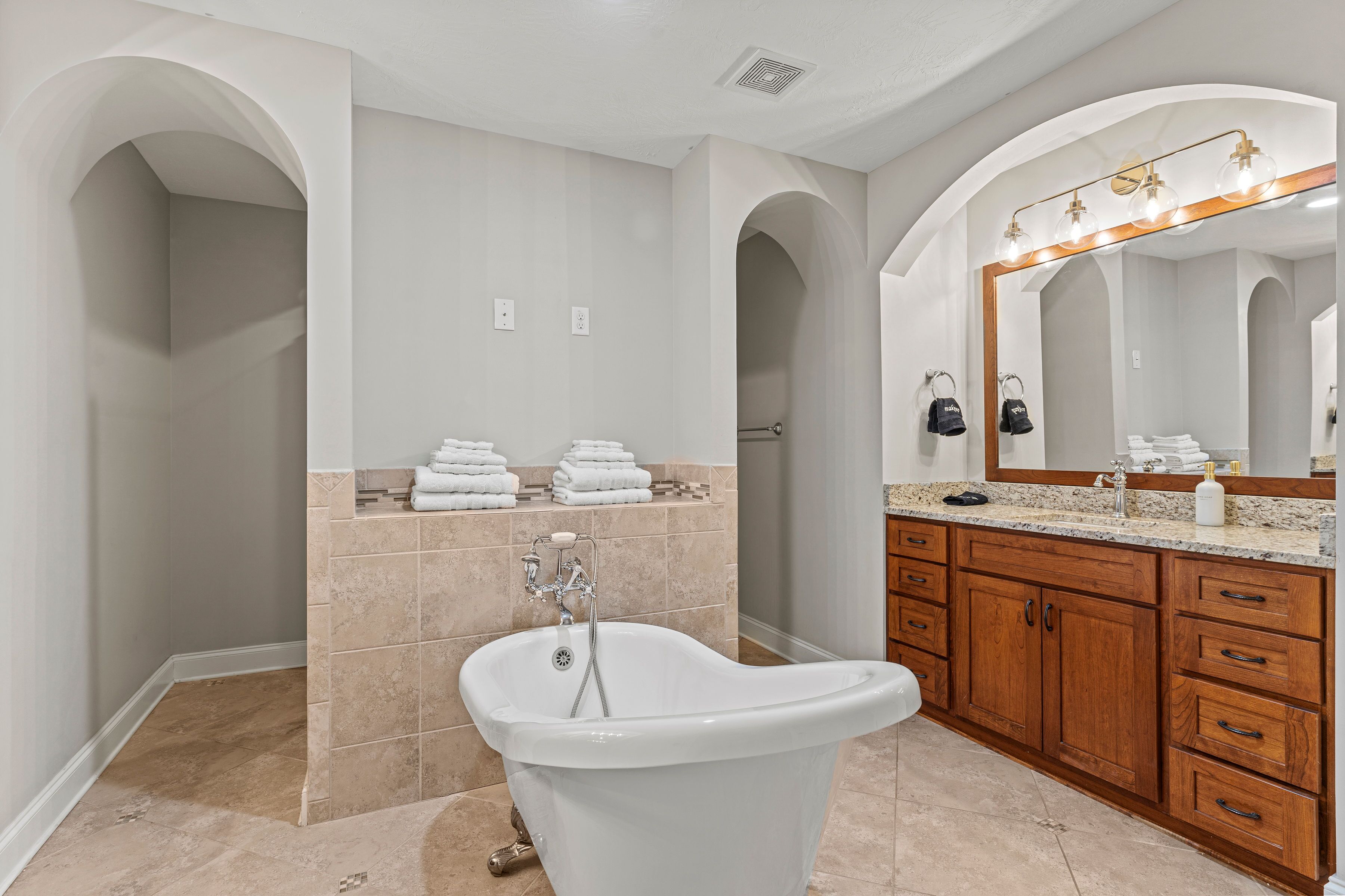 A bathroom with a freestanding bathtub, wooden vanity with a large mirror, and a towel rack with neatly folded towels.