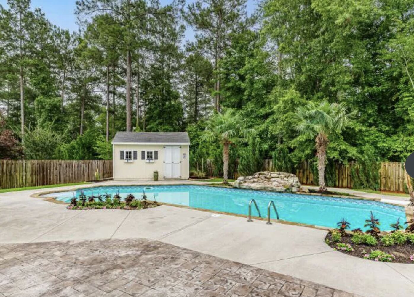 Un jardin avec une piscine, un petit abri de jardin et une clôture en bois.