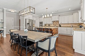 A modern kitchen with white cabinetry, a central island, and a dining area with a wooden table and chairs.