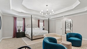 Een slaapkamer met een bed, een stoel, een nachtkastje, een spiegel en een kroonluchter.