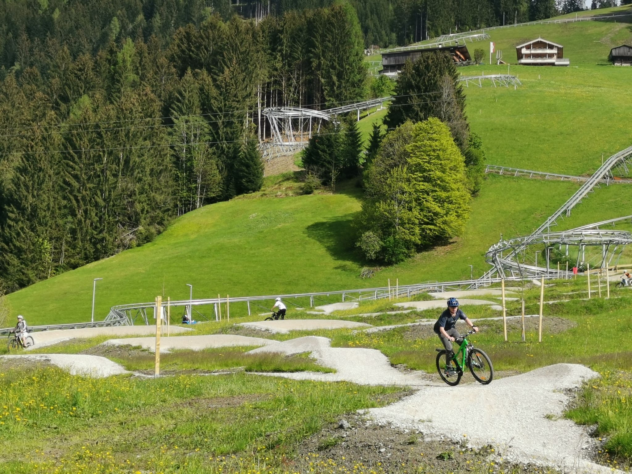 A mountain biking trail with a single rider, surrounded by green hills and trees.