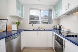 A modern kitchen with white cabinets, a blue countertop, a stainless steel dishwasher, and a window with a view of buildings.