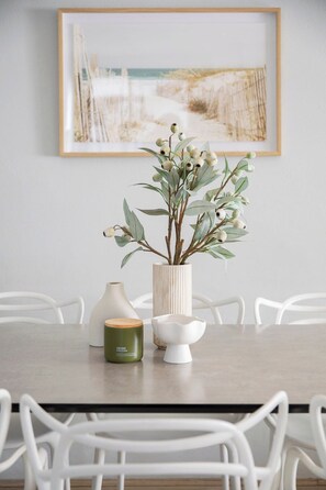 Une table à manger ornée d’un vase rempli de feuillage vert, d’un bol blanc et d’une bougie verte.