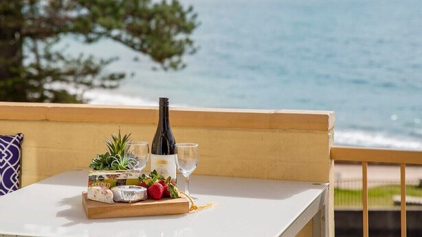 Une table avec une bouteille de vin, des verres, du fromage et des fraises, sur un balcon donnant sur la mer.