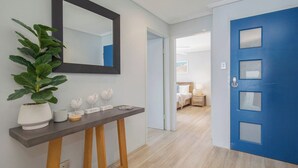 A hallway with a blue door, a potted plant, a mirror, and a bedside table with a lamp. - Oceans at Terrigal, a Beachfront Oasis (Terrigal)