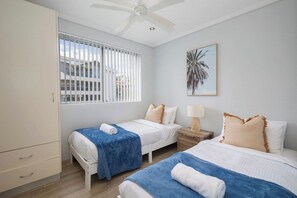 A hotel room with two beds, a wardrobe, a window with blinds, a ceiling fan, and a framed picture on the wall. - Oceans at Terrigal, a Beachfront Oasis (Terrigal)