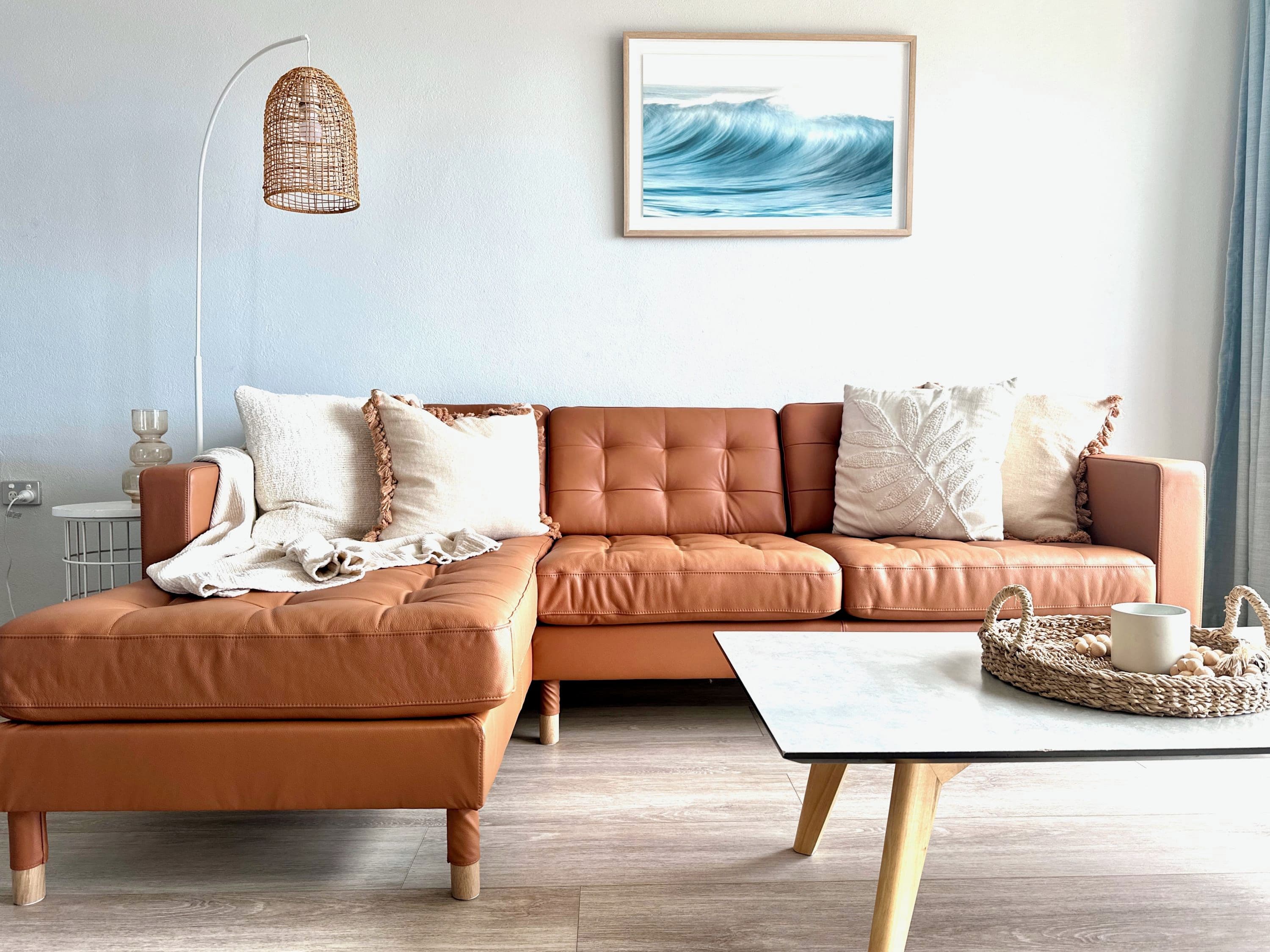 A modern living room with a brown leather sofa, a white table, and a framed artwork of waves.