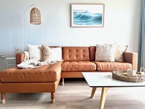 A modern living room with a brown leather sofa, a white table, and a framed artwork of waves.