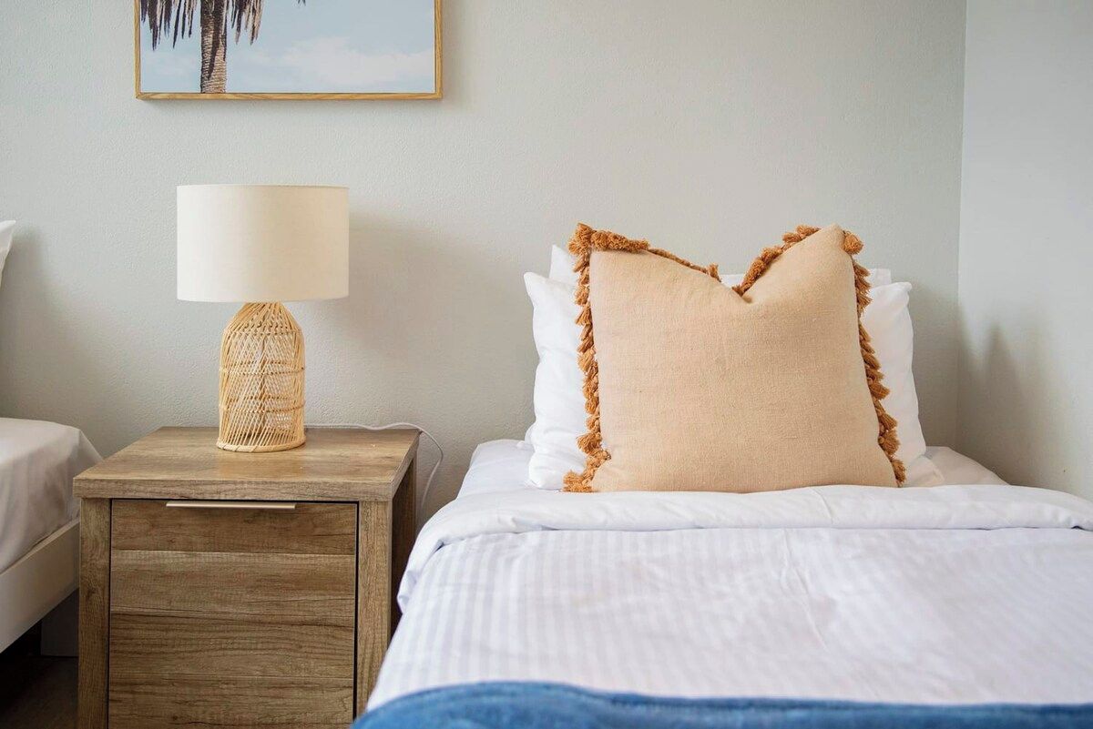 Een hotelkamer met een bed, een nachtkastje met een lamp en een aan de muur hangend schilderij.