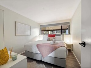 Ein modernes Schlafzimmer mit Bett, Nachttisch und Blick durch ein Fenster.