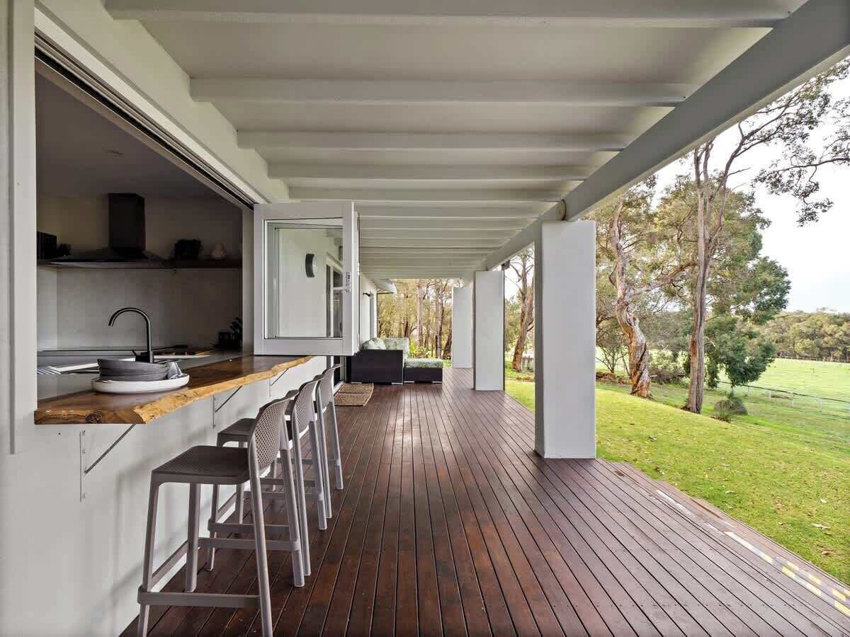 An outdoor kitchen area with a bar seating arrangement, a wooden deck, and a view of a grassy landscape.