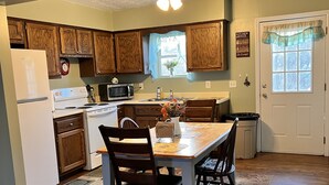Una cocina con armarios de madera, refrigerador, estufa y una mesa de comedor con sillas.