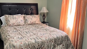 Un dormitorio con cama, mesita de noche, lámpara y cortinas.
