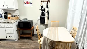 Una cucina compatta con un forno a microonde su un ripiano in legno, un tavolo da pranzo con tovaglia a righe e un appendi-asciugamani da cucina a sospensione.