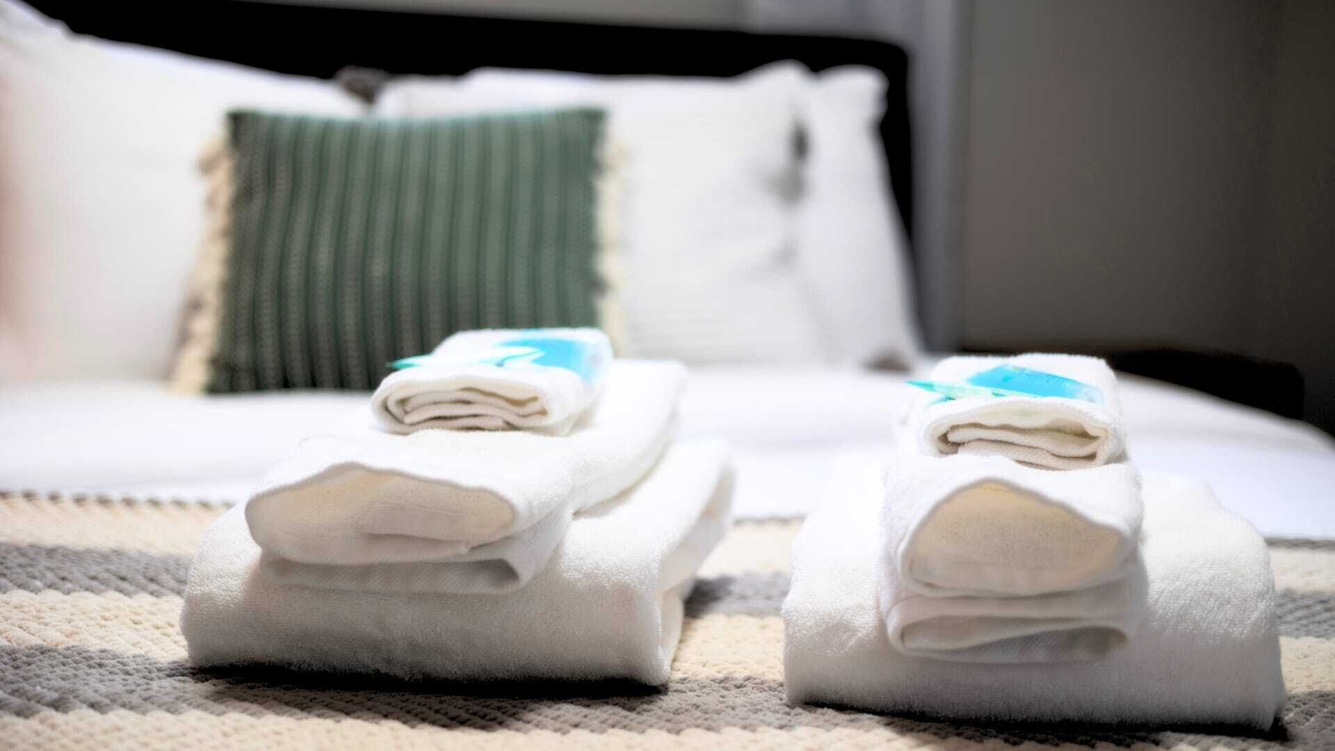 Un lit bien fait, avec du linge de lit blanc et un coussin vert.