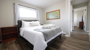 Una camera d'albergo con un letto, un comodino in legno, un quadro appeso al muro e un corridoio che conduce a un'altra stanza.