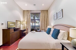 A hotel room with a large bed, a TV on a wooden cabinet, a small table, and a window with curtains. - 1B-AnantaraSouth-G02 by bnbmehomes (Dubai)