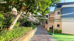 A pathway flanked by greenery and buildings with a brick-paved walkway. - 1B-AnantaraSouth-G02 by bnbmehomes (Dubai)