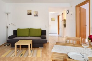 A living room with a sofa, a small table, a dining table with chairs, and a glass of water.