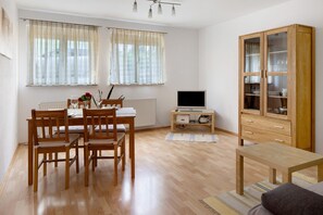 A room with a dining table, chairs, a TV, a cabinet, and a radiator.