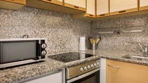 A kitchen with a microwave, stove, sink, granite countertop, and wooden cabinets. - Apartment 'Ferienwohnung Glöckler' with Shared Garden and Wi-Fi (Freiburg im Breisgau)