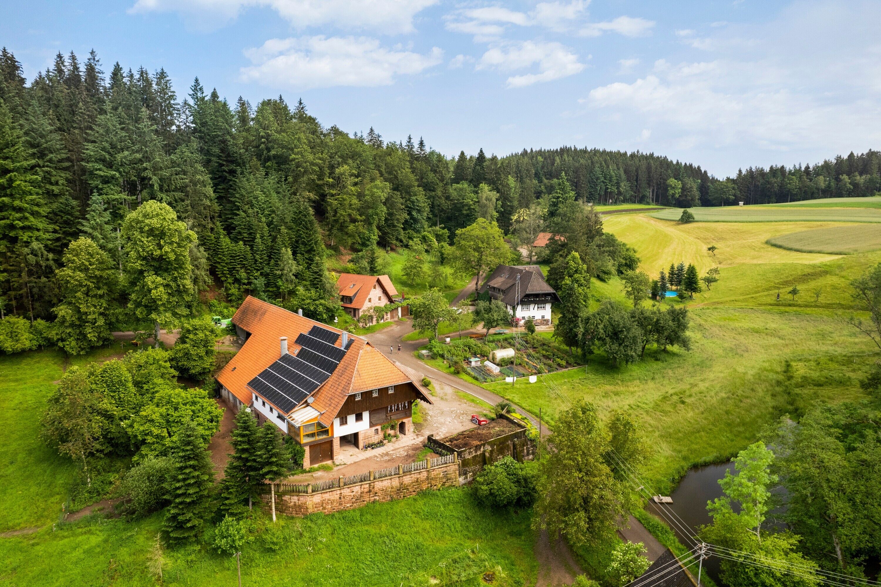 Een landhuis met een zonnepaneel op het dak, omringd door weelderige begroeiing en een beekje.