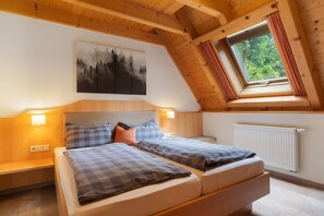 Une chambre avec un plafond de style industriel, un lit avec une literie à carreaux, une table de chevet, une lampe fixée au mur, un radiateur et une fenêtre avec des rideaux.