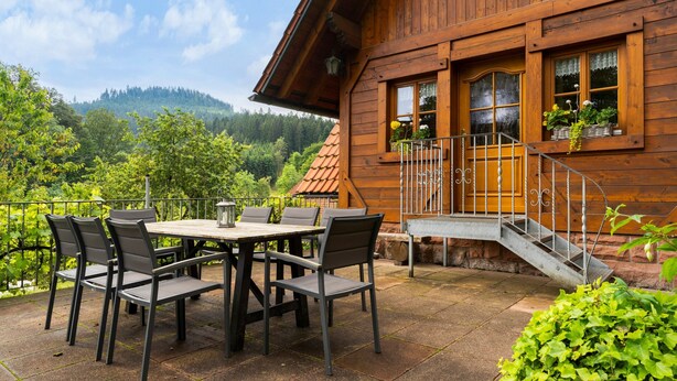 A wooden cabin with a patio table and chairs, a staircase, and a view of a forested hillside. - Holiday Home 'Hexenhäuschen' with Mountain View, Private Terrace and Wi-Fi (Wolfach)