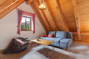 Une pièce mansardée chaleureuse avec un plafond en bois, un canapé bleu, un fauteuil poire et une petite table.