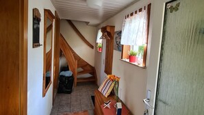 Ein Flur mit einer Holztreppe, einer Bank mit einer Vase und einer Tür mit beschlagenem Glas.