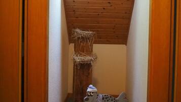 Una habitació amb sostre inclinat, una finestra, un arbre rascador per a gat i un gosset de joguet.